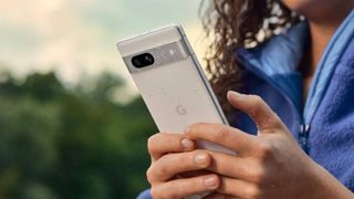 Woman holding Pixel 7a in snow with water droplets on it 