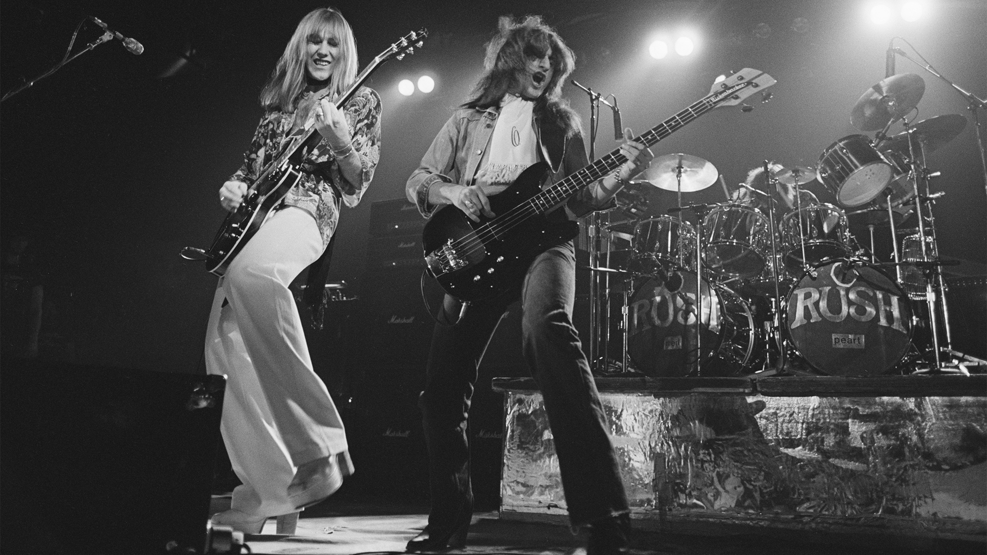 Alex Lifeson (left) and Geddy Lee performing with Canadian progressive rock group, Rush, at the Civic Center in Springfield, Massachusetts, during the band's All The World's a Stage tour, 9th December 1976. Neil Peart is on drums (right).