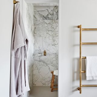 a neutral bathroom with marble floor and wall tiles and a shower area with brass fittings