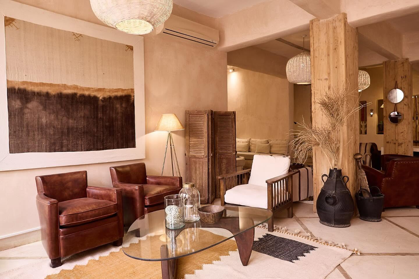 A hotel lounge decorated with sandy tones and furniture, including a patchwork rug, leather armchairs, and dark large vases.
