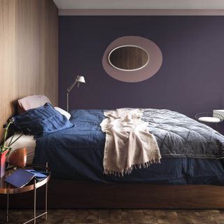 Dark purple bedroom with wooden accent wall, with Heartwood and Blacberry Bush paints by Dulux and round oval mirror