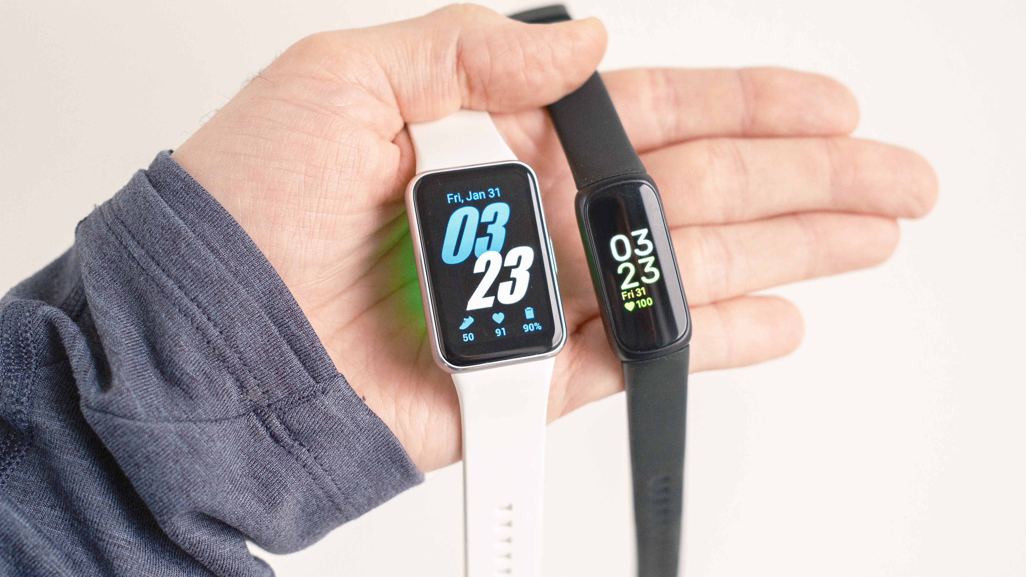 Close-up of the Samsung Galaxy Fit3 next to the Fitbit Inspire 3 in a user's hand