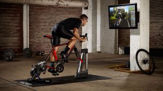 Cyclist on a road bike fitted to a Wahoo Kickr and Kickr Climb whilst riding on Zwift in a warehouse gym