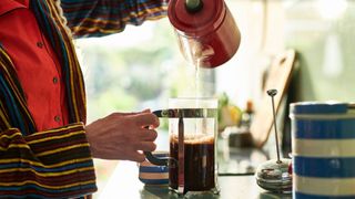 Woman pouring black coffee from a French press coffee maker into mug