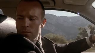 Jason Statham as Frank Martin glancing behind him while driving in The Transporter