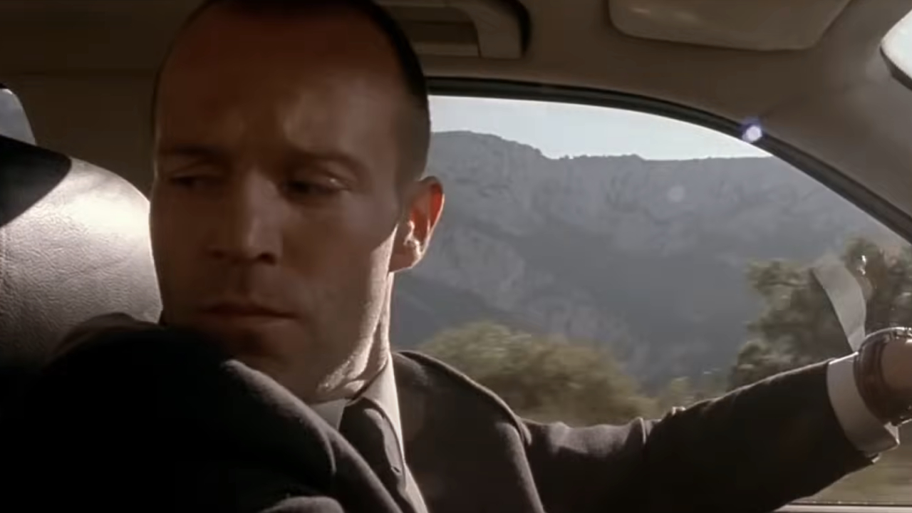 Jason Statham as Frank Martin glancing behind him while driving in The Transporter