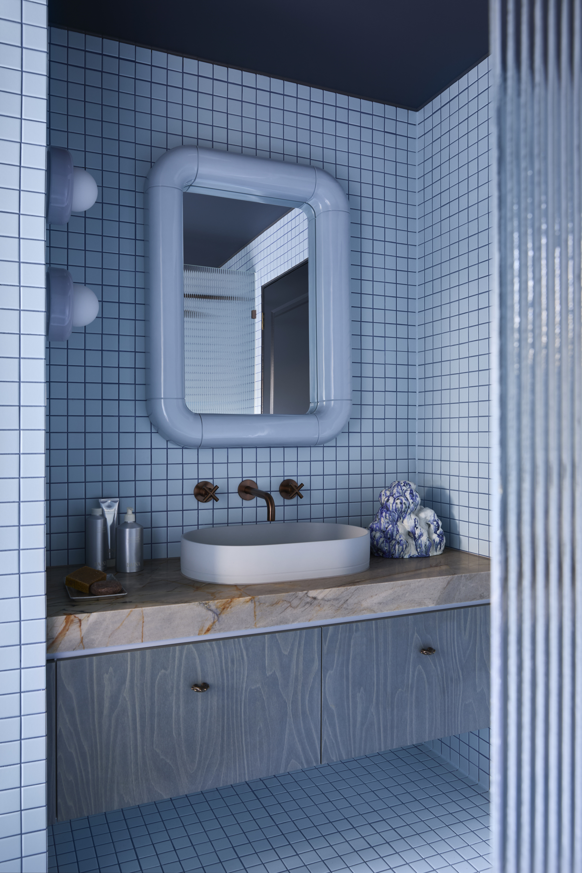 a blue bathroom with small square tiles, a stone vanity and wall sconces