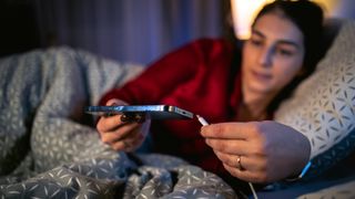 A woman lying in bed plugging in her iPhone.