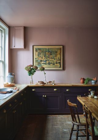 How to paint kitchen cabinets, with Farrow and Ball painted midnight blue cabinetry in a plaster pink kitchen with wooden floorboards and countertops.