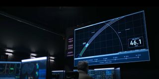 a darkened mission control room with a tracking screen