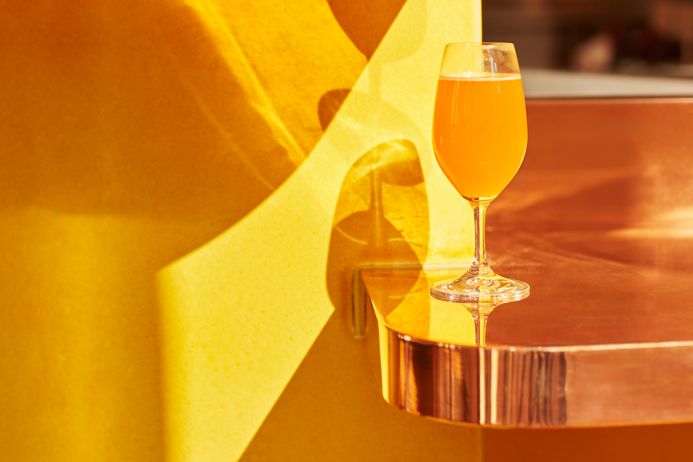 An orange-tinted drink sits on a bronze, sleek bar counter.