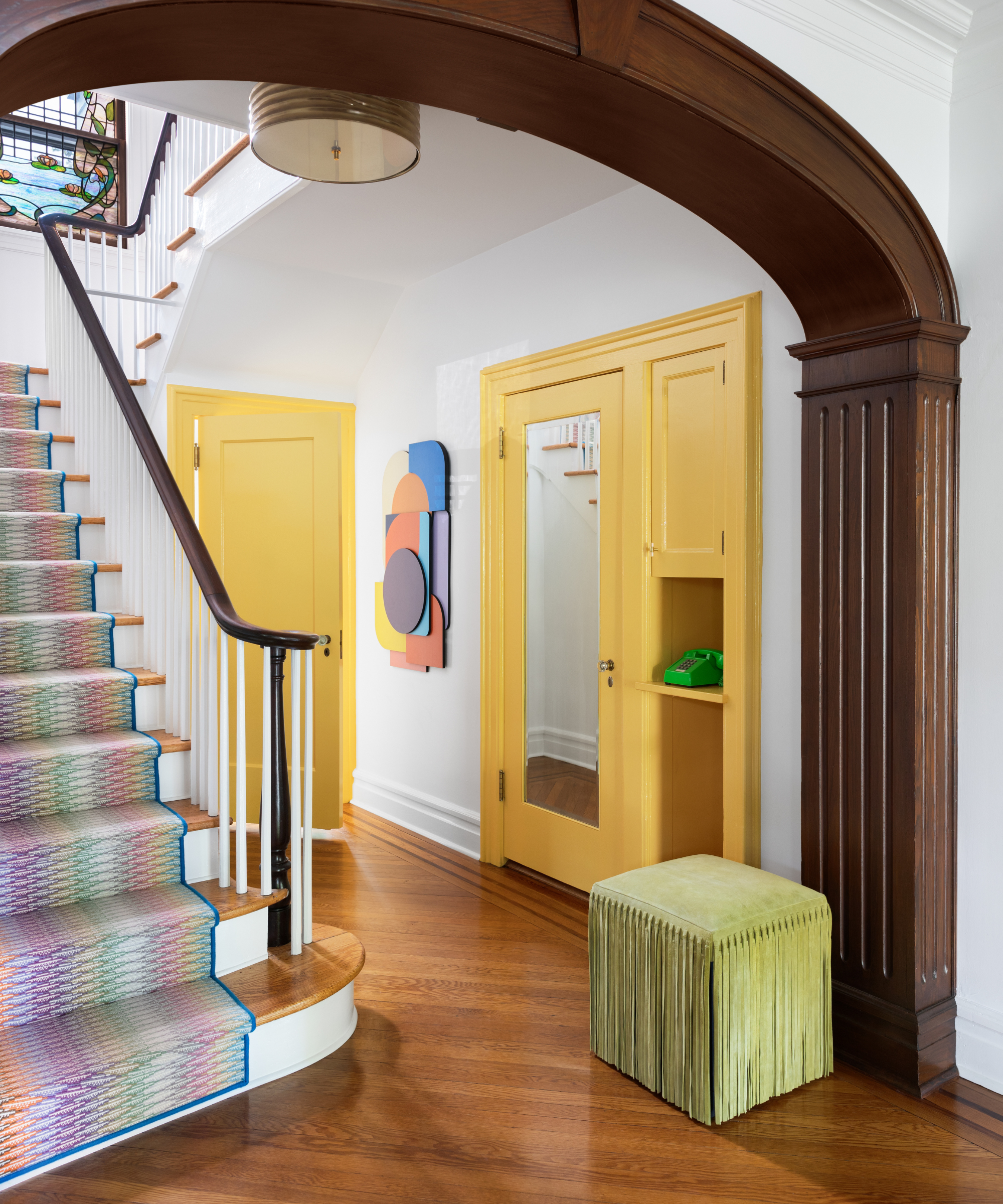 an entryway with a staircase with a colorful staircase runner rug, a green ottoman, and two yellow accent doors