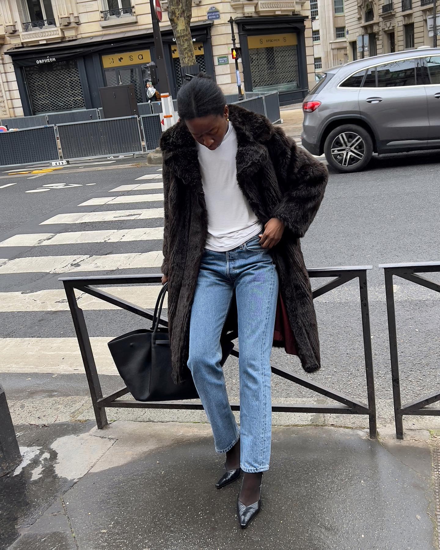 A woman wears a fur jacket, white shirt, stovepipe jeans, and black pumps.