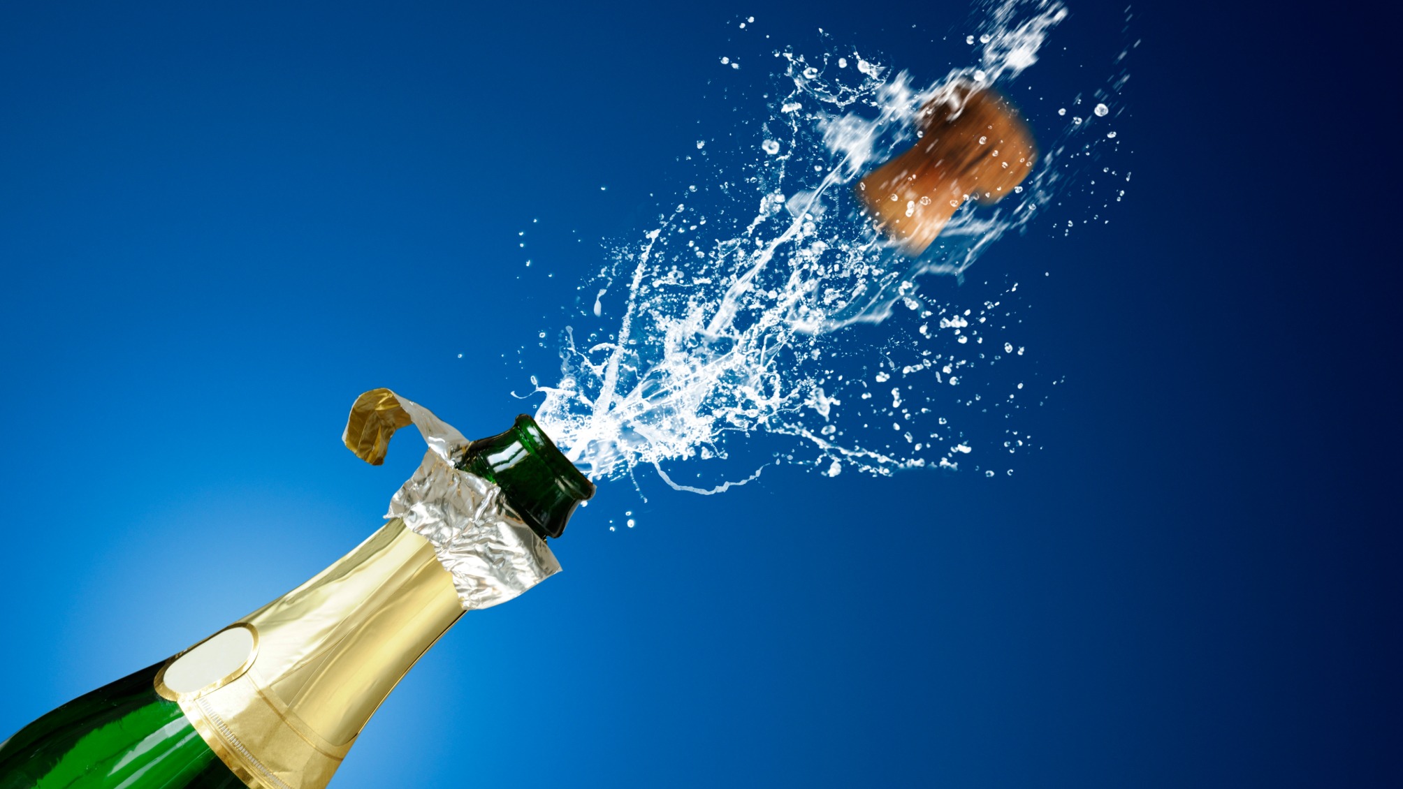 Close up of champagne popping and spraying against blue background