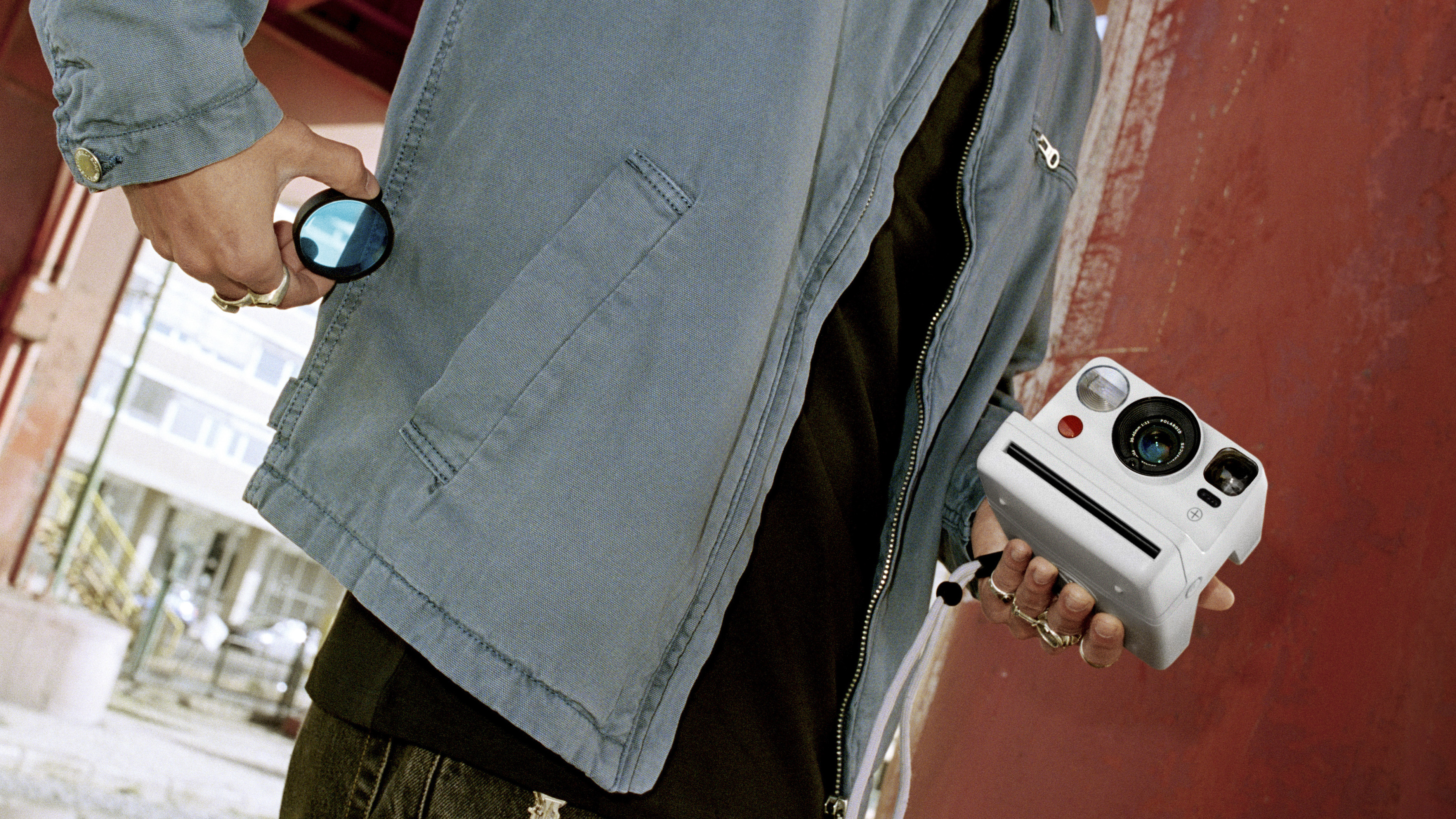 Man holding Polaroid Now 3+ instant camera and taking a lens filter out a pocket