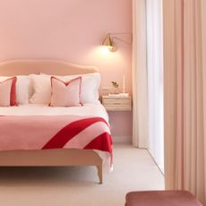 an all-pink Barbiecore bedroom with pink and red bedspread, pink walls, white curtains, and walls painted in Lick paint
