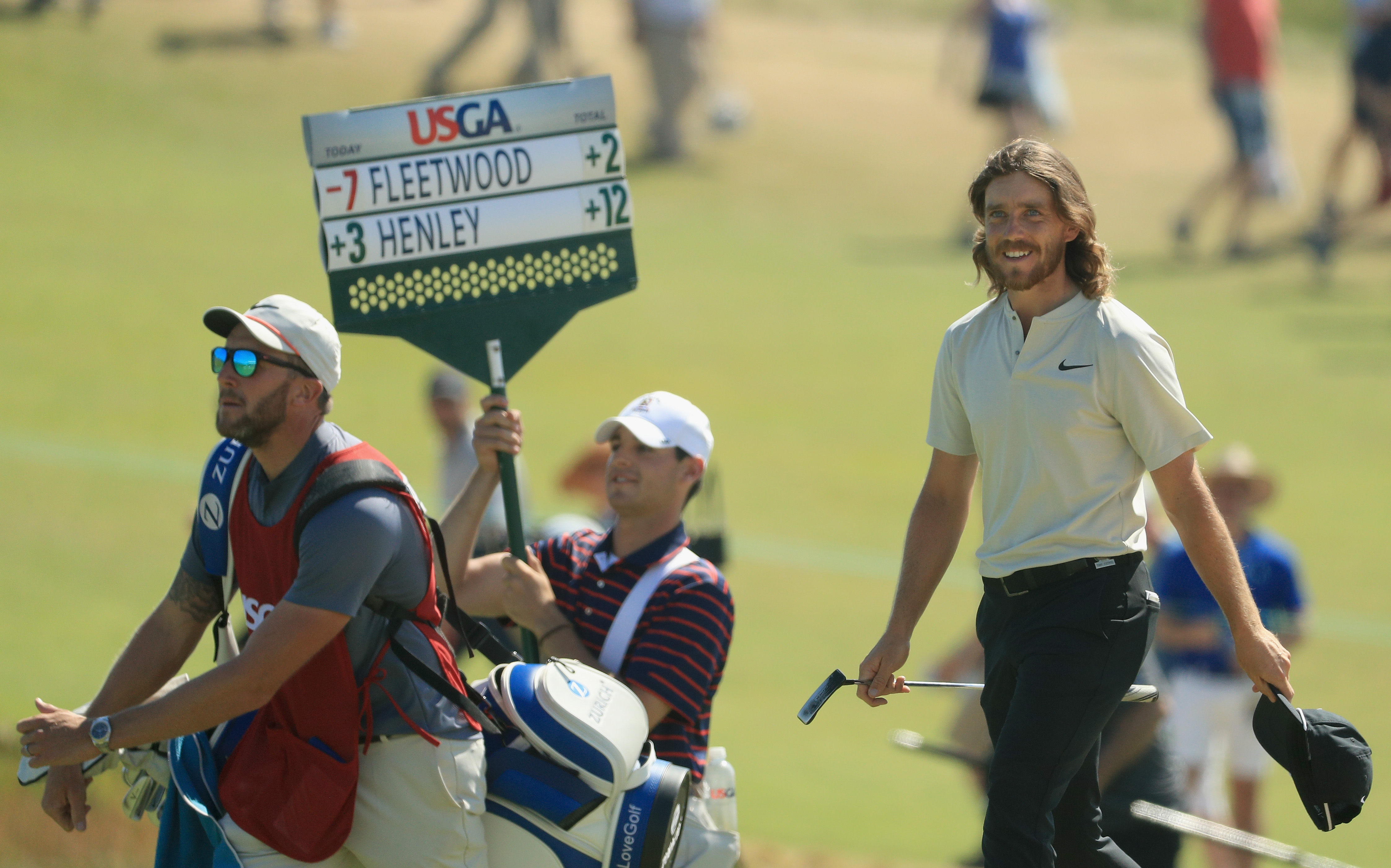 Tommy Fleetwood walks down the 18th at Shinnecock Hills during the final round of the 2018 US Open with a scoreboard being carried showing his seven-under total in the background