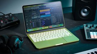 An Apple MacBook Neo on a desk with an audio interface, studio monitors, headphones, and two MIDI controllers. Displayed on the screen is the Logic Pro DAW