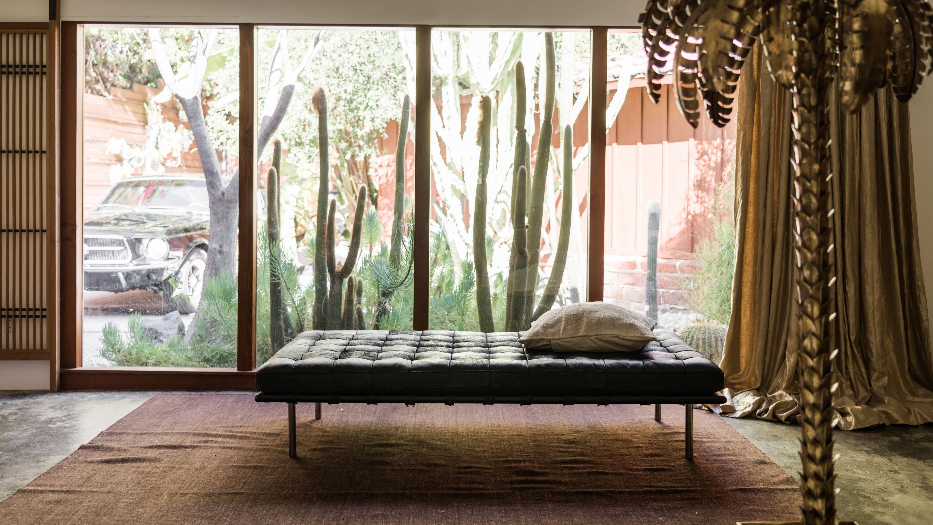 Image of a black leather daybed in a large, minimalist entryway. The back wall is made of windows and there are cacti outdoors.