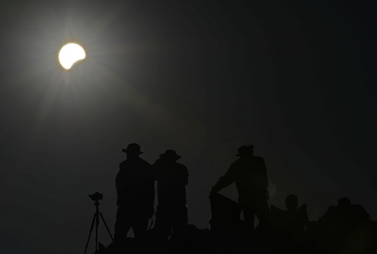 People watch as the moon appears to cover the sun during the partial phase of an annular eclipse of the sun May 20, 2012 from the Pueblo Bonito ancient building at Chaco Culture National Hist