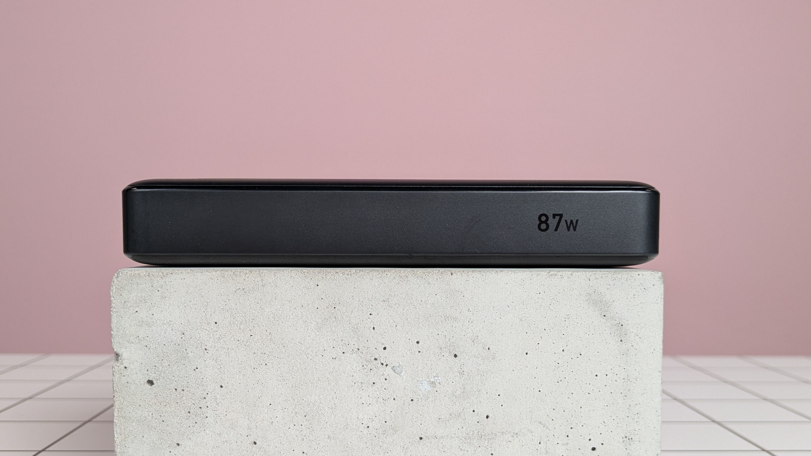 Anker 20,000mAh 87W Power Bank leaning on plinth on desk, with pink background