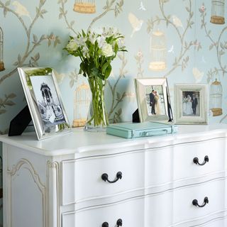 room with wallpaper on wall photo frames and glass vase