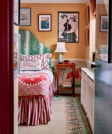 small eclectic bedroom painting in a soft orange with a striped bed skirt, green patterned headboard and a large rug