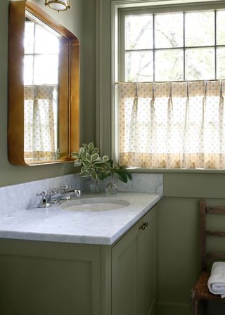 A bathroom with sage walls, marble sink and brass mirror