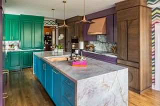 A colorful kitchen with green cabinets on one side, purple and brown on the other, and blue cabinets on the kitchen island with a pinkish/purple countertop.