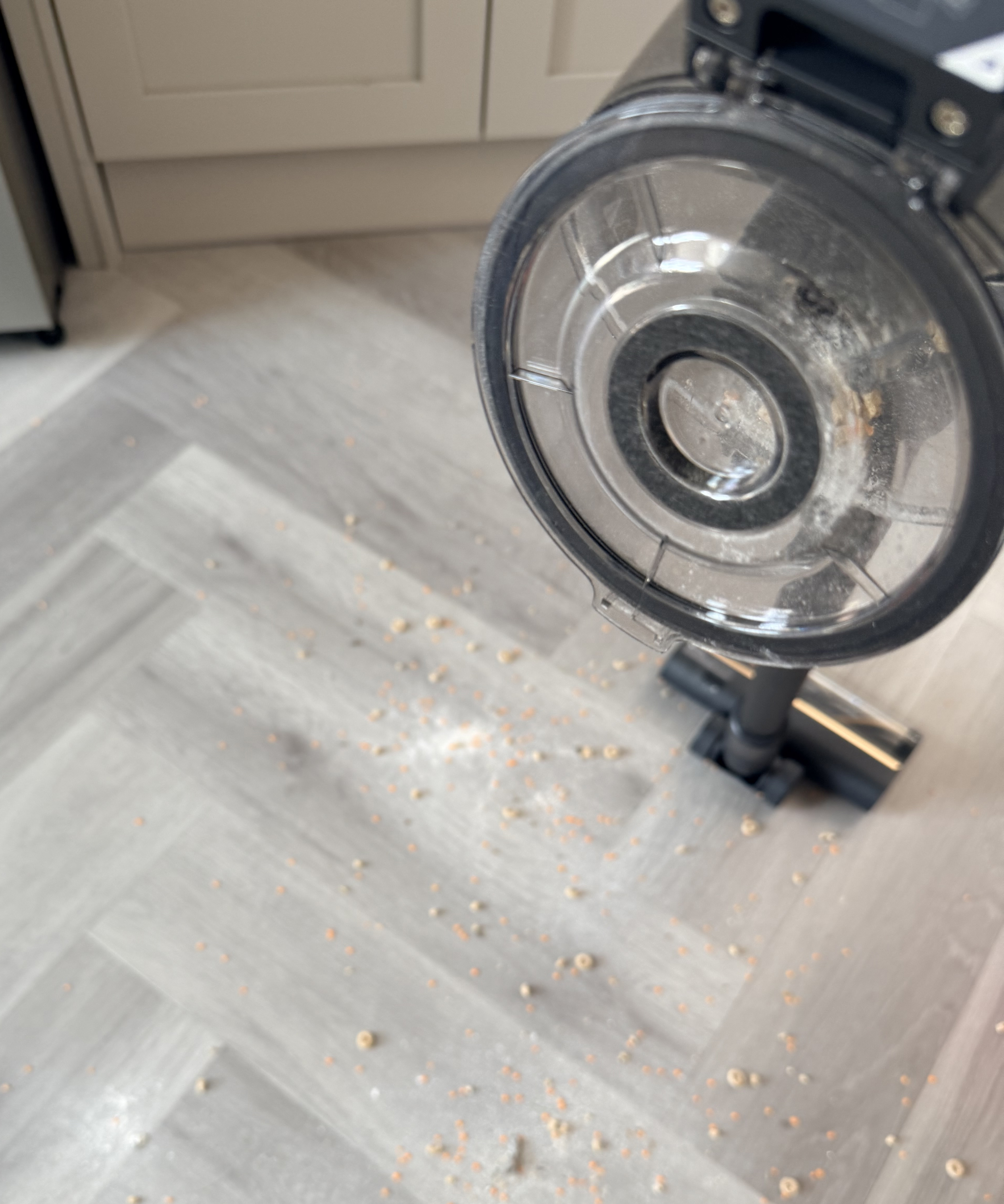 Dreame R10 Pro dust cup open above scattered cereal and lentils on a kitchen floor