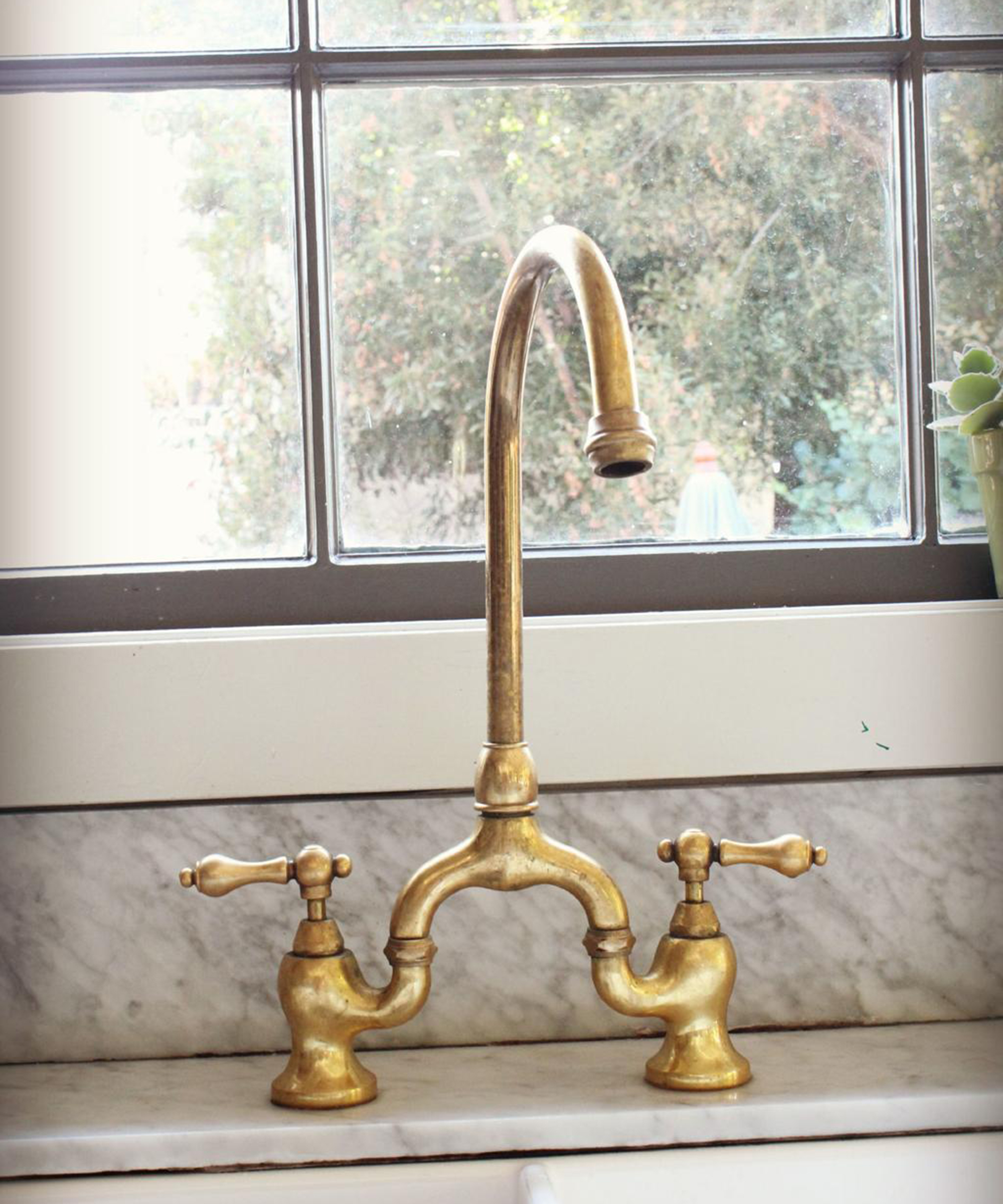 unlacquered brass faucet on a marble counter in front of a window