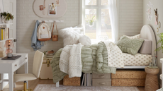 a dorm room with a twin bed and a green comforter, storage boxes underneath, a side table, and a desk with a chair