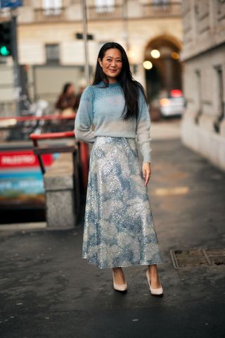 A woman at Milan Fashion Week's Fall 2025 Street Style in a shimmery blue maxi skirt and blue and white crewneck sweater