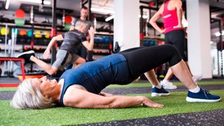 Woman performs glute bridge exercise in a busy gym