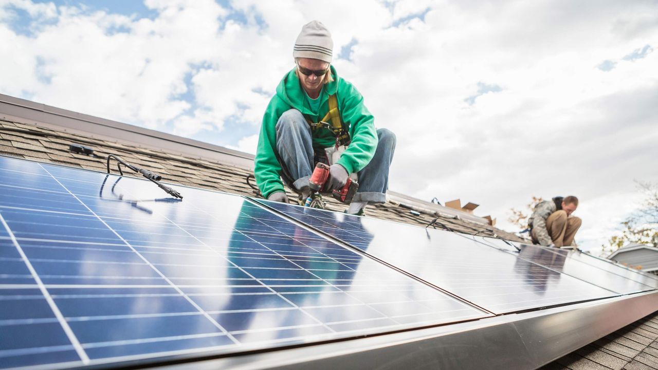 A woman uses a drill to attach a solar panel to a home&amp;#039;s roof.