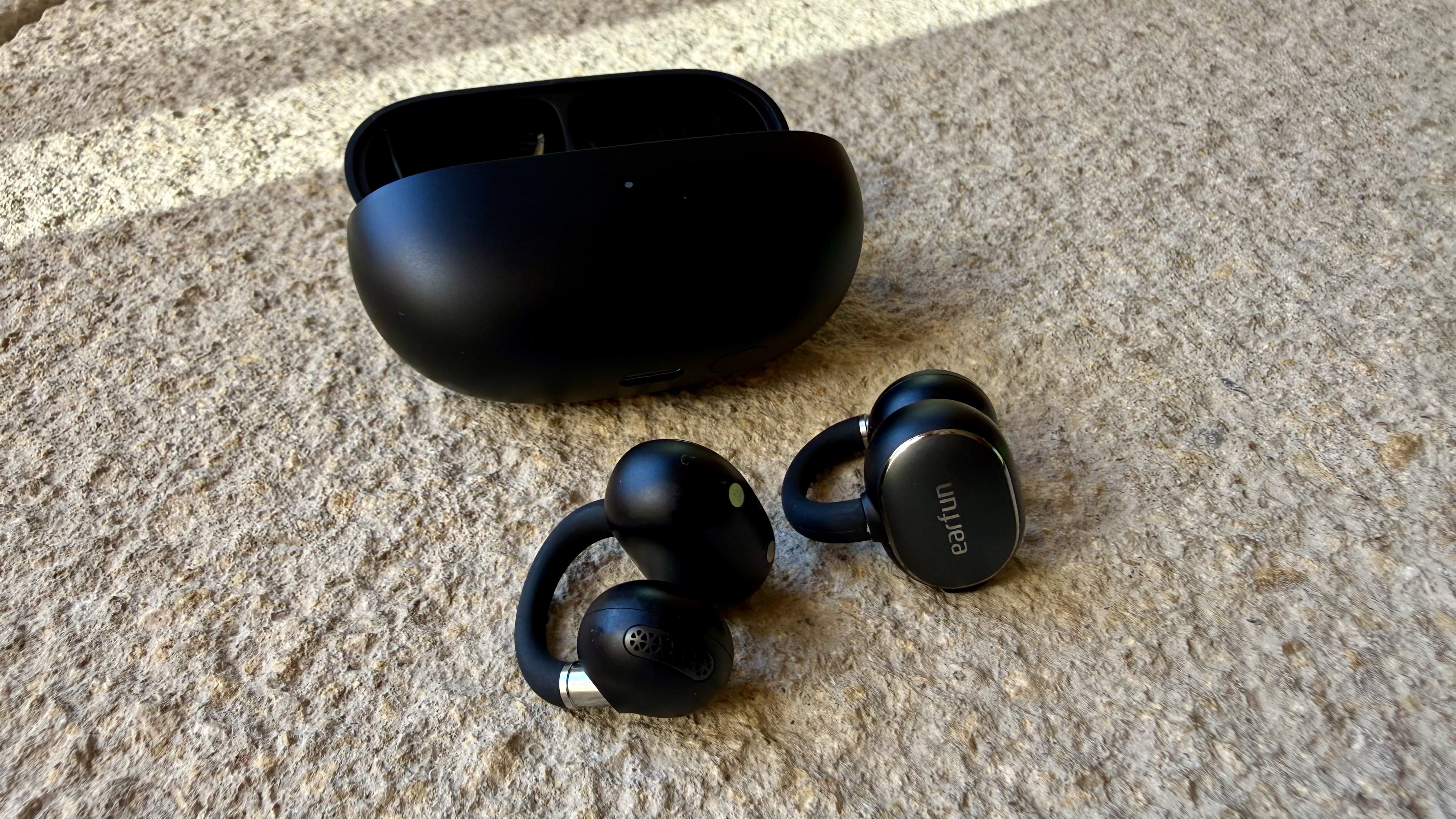 The EarFun Clip 2 earbuds on a stone surface next to their charging case