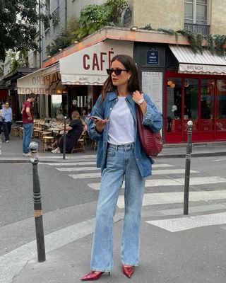 Fashion influencer @leasy_inparis in Paris wears an anti-trend outfit with a denim shirt, jeans, a white t-shirt, a burgundy ash and burgundy-colored pumps.