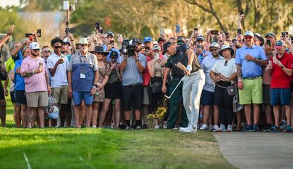 Spieth strikes a shot from the cart path with a number of fans looking on