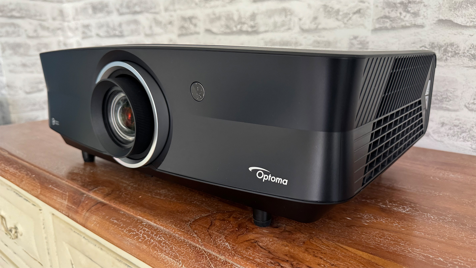 Optoma UHZ68LV home cinema projector on wooden sideboard in front of grey brick wall