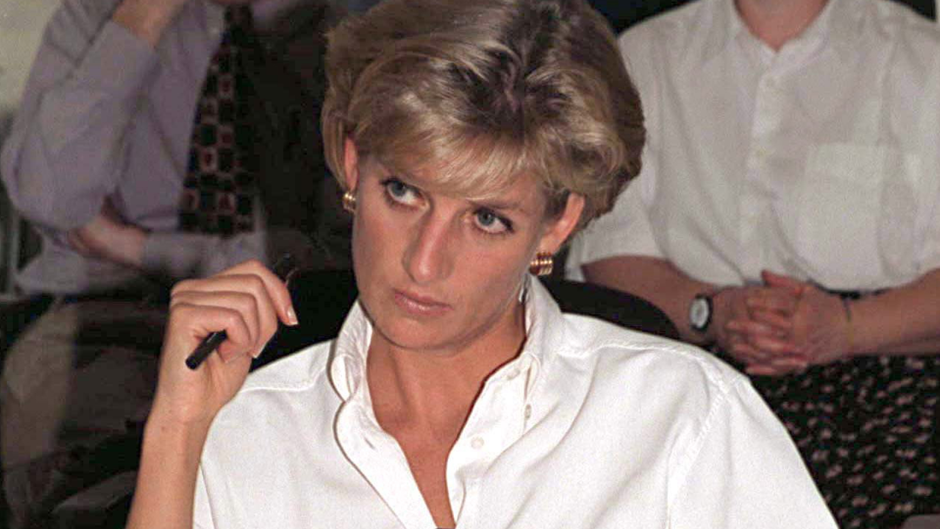 Princess Diana wears a white button-down shirt and looks pensive