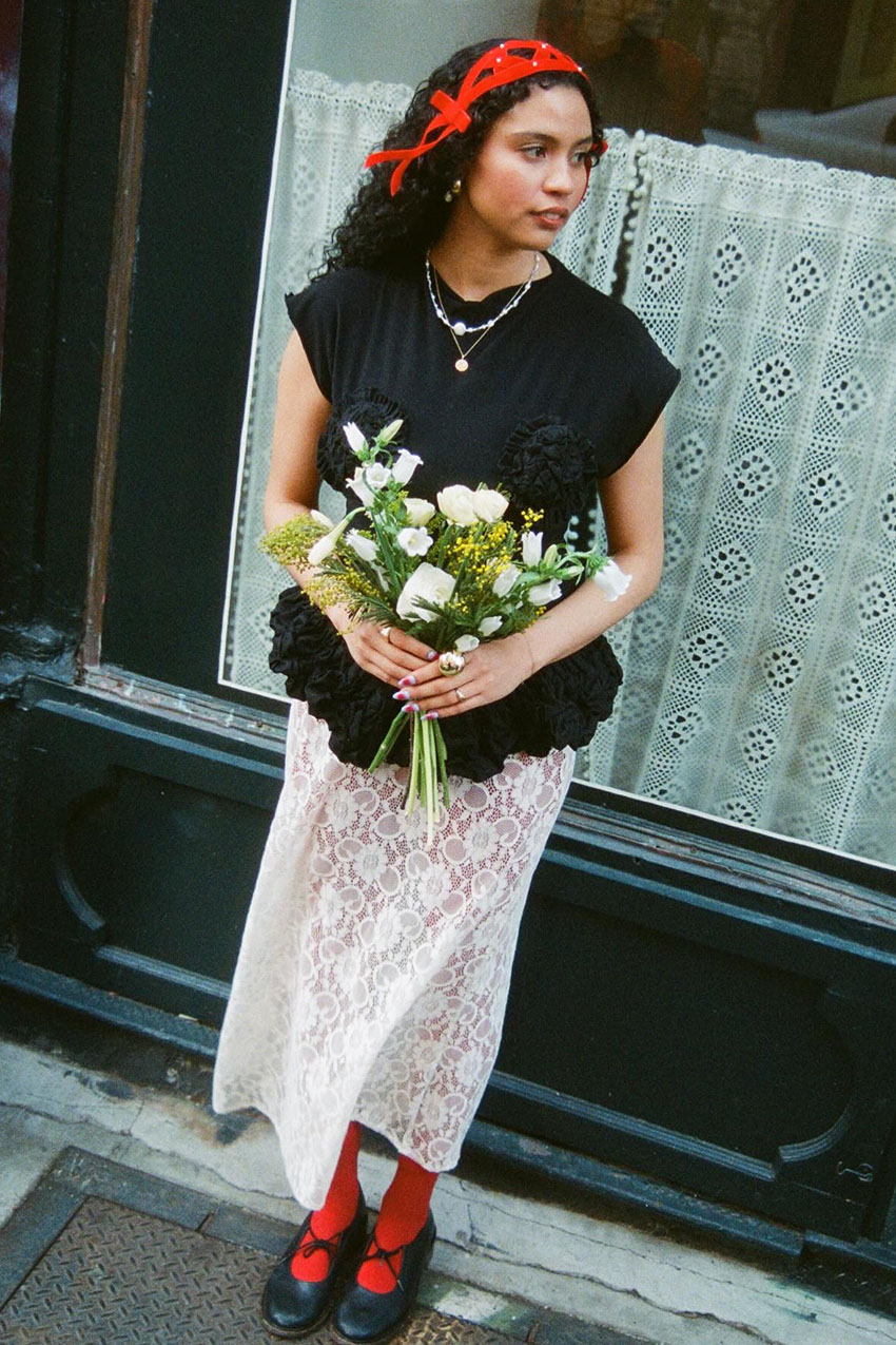 a woman wearing a black top, white lace sheer skirt, red tights, and black Mary Janes