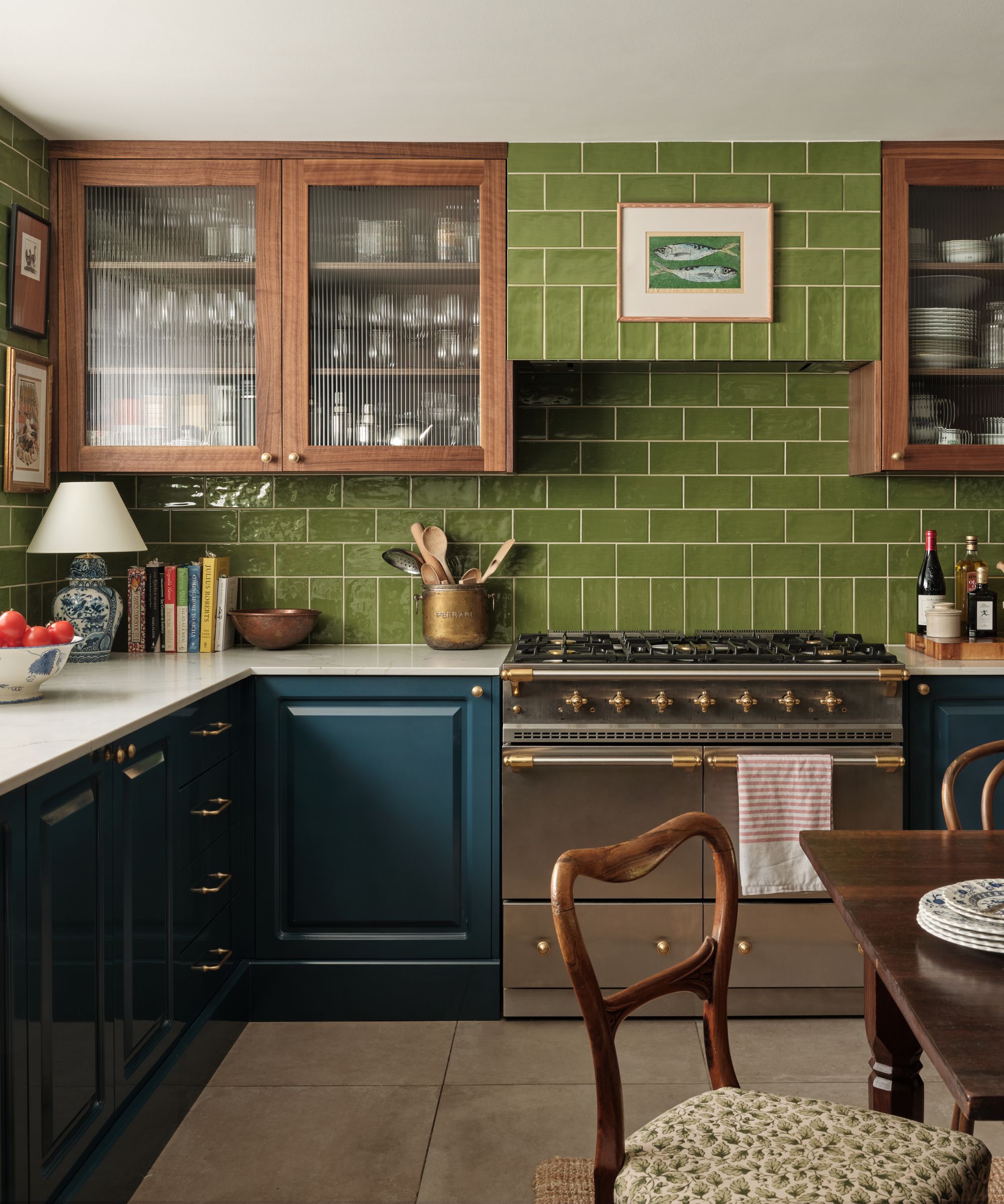 english kitchen with dark teal lower cabinets, upper glass fronted wooden cabinets, green tiled backsplash and cooker hood and silver range oven
