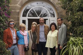 A cast shot from The Madame Blanc Mysteries Christmas special 2023, showing Robin Askwith as Jeremy, Sue Holderness as Judith, Sally Lindsay as Jean, Steve Edge as Dom, Sue Vincent as Gloria and Alex Gaumond as Caron, all standing outside the door of a grand-looking building, bordered by lush vegetation
