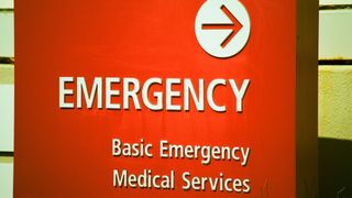 A red sign indicates the direction to the emergency department at a hospital.