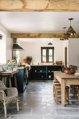 stone floor in country kitchen with dark blue cabinets, wood dining table and wood worktops