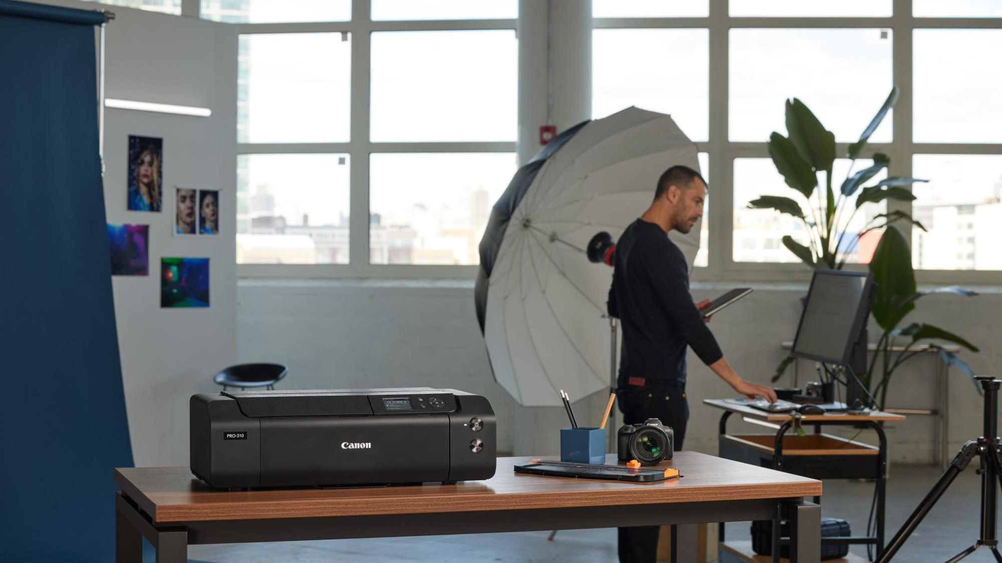 A canon printer sits on a table in the foreground as a photographer works in a studio.