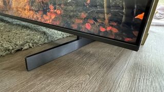 TCL 98Q9BK Mini LED TV on wooden floor and green rug, close up on bottom right corner of screen