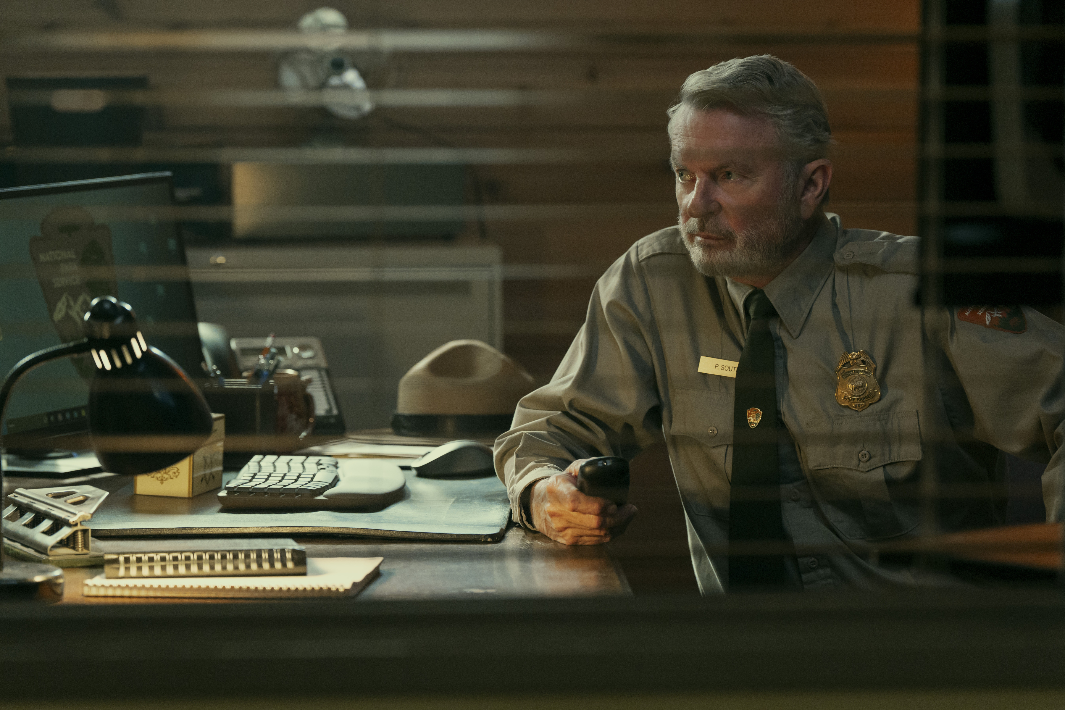 sam neill as a park ranger sitting in his office in the tv show untamed