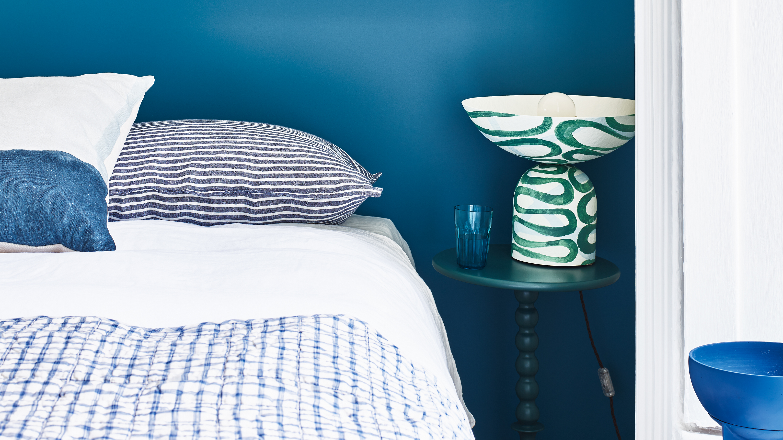 A bedroom with a dark blue wall and blue and white bedding on the bed