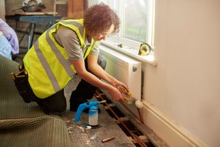 A female plumber wearing a hi vis vest installing copper pipe for a radiator 